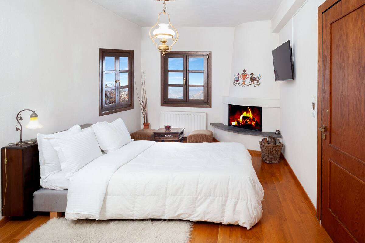 A bedroom with a bed, a fireplace, a television, and a wooden door.