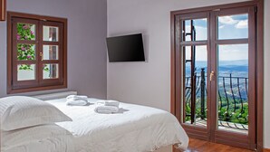 Ein Schlafzimmer mit einem großen Bett, einem an der Wand montierten Fernseher und einem Balkon mit Blick auf die Landschaft.