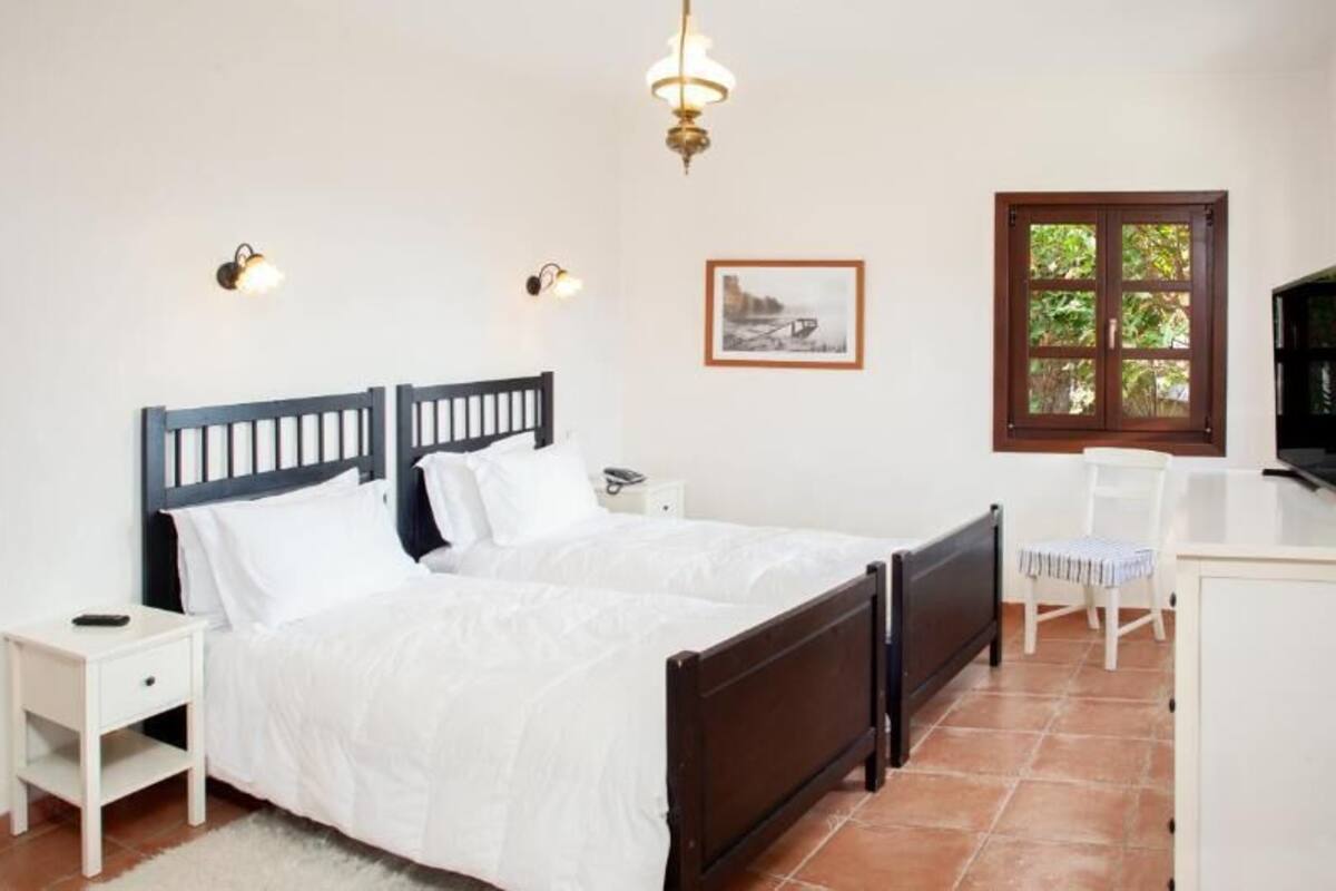 A bedroom with a double bed, bedside tables, a desk, a chair, a window, and a door.