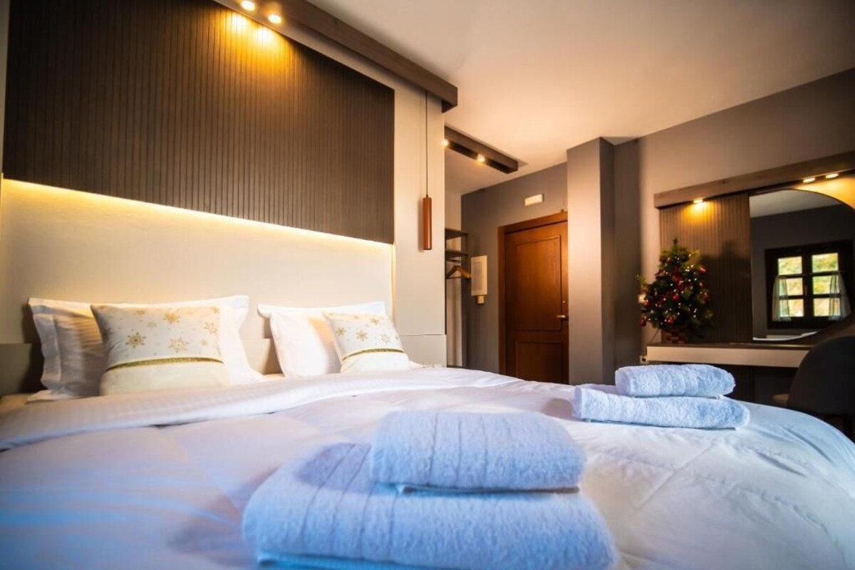A hotel room with a large bed, a wooden headboard, a desk, a chair, and a Christmas tree.