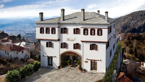 Ein zweistöckiges Hotel mit Steinaußenwand, mehreren Schornsteinen und Blick auf die Stadt im Hintergrund.