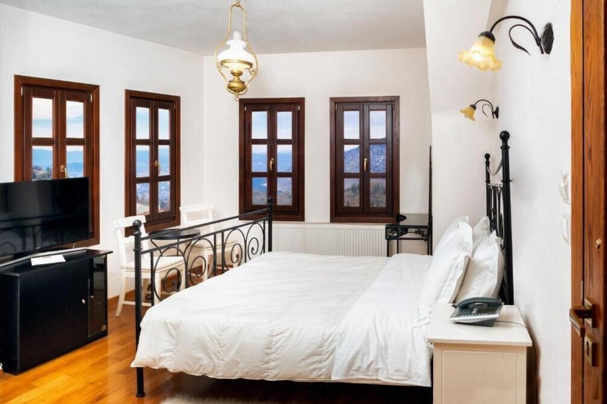 A bedroom with a bed, a desk, a chair, a TV, and a window with a view.
