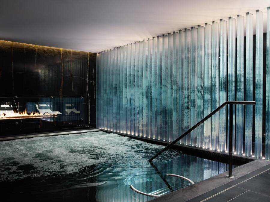 Un espace piscine intérieur moderne, doté d’un mur en verre, d’une rambarde en métal et d’un foyer.