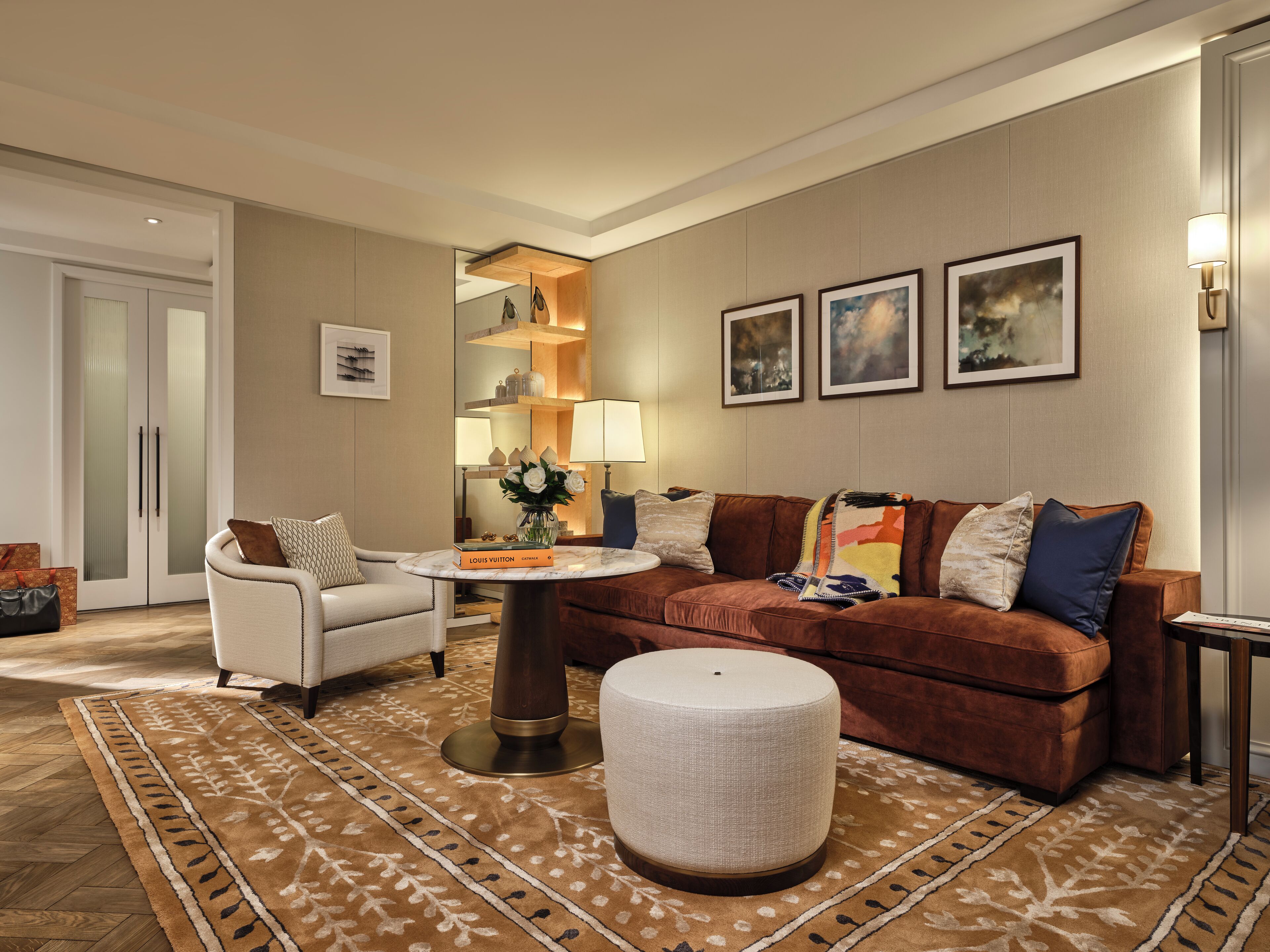 Un salon moderne avec un canapé en cuir marron, un fauteuil blanc, une table basse ronde et un tapis à motifs.