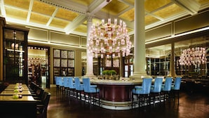 A bar area with a central column, multiple seating arrangements, and a chandelier. - Corinthia London (London)