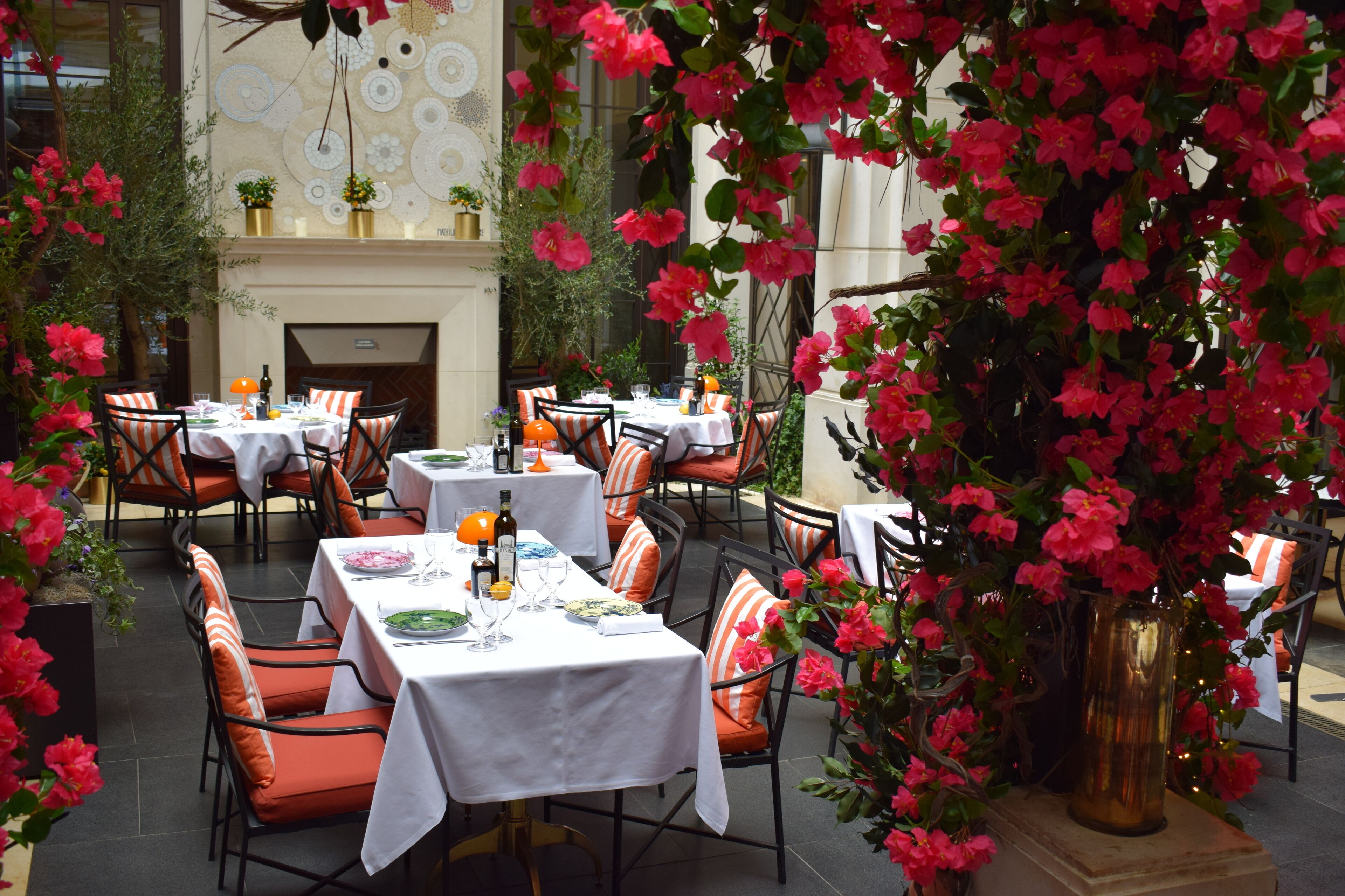 A restaurant with tables set for dining, surrounded by lush greenery and vibrant flowers.