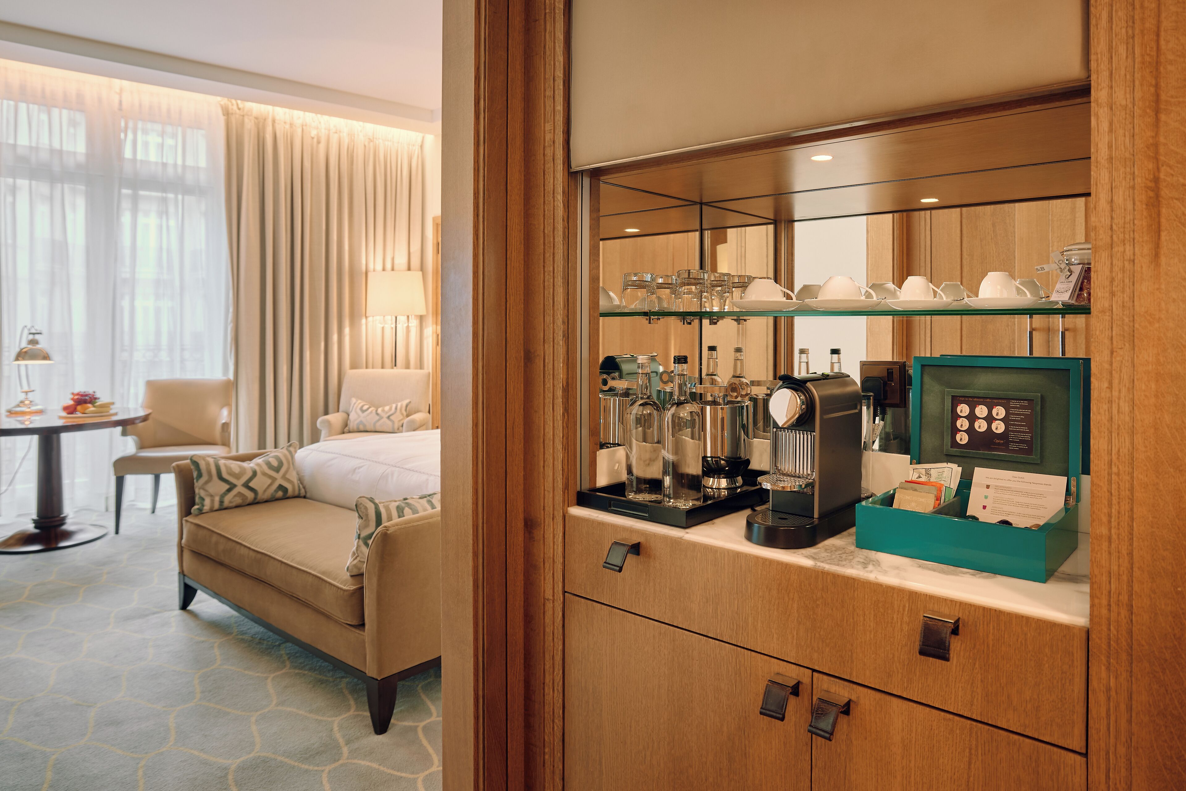 Habitación de hotel con cama, sofá, zona de café y escritorio con lámpara.