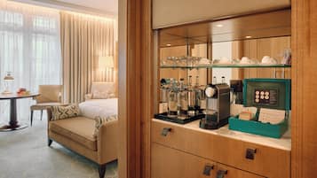 Habitación de hotel con cama, sofá, zona de café y escritorio con lámpara.