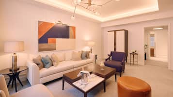 A modern living room with a sofa, coffee table, and armchairs. There is a painting on the wall and a chandelier above the seating area.