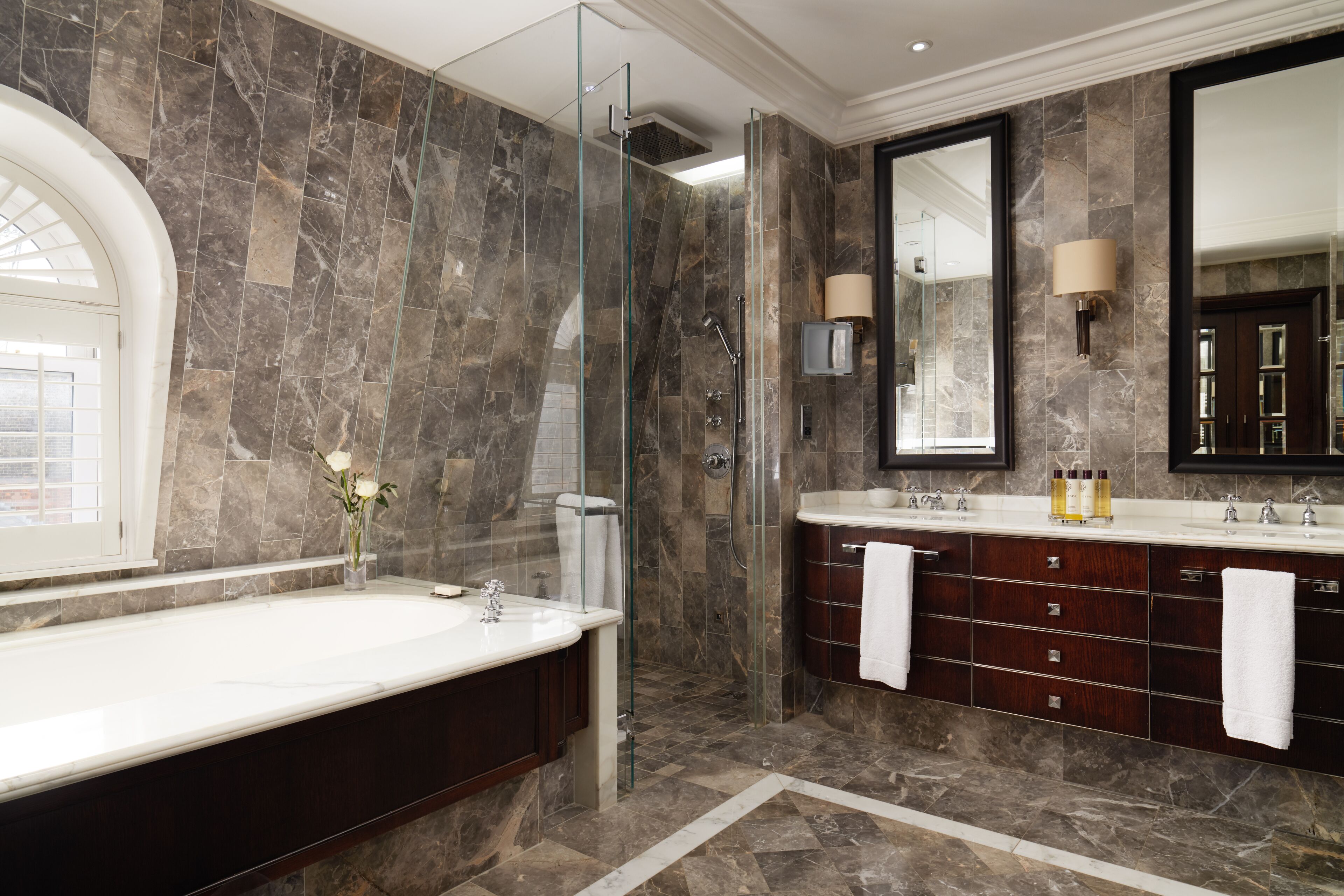 A modern bathroom with a large bathtub, a glass-enclosed shower, and a vanity with a mirror and multiple drawers.