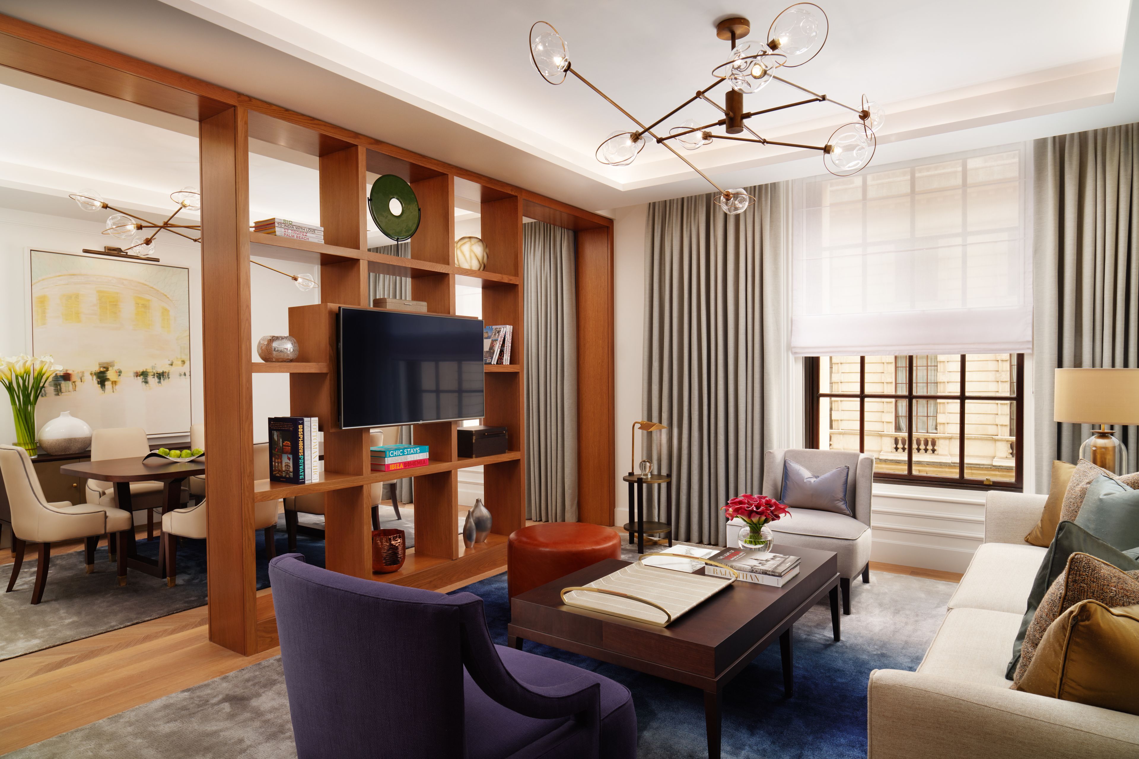 A modern living room with a television, bookshelves, a dining area, and a large window with curtains.