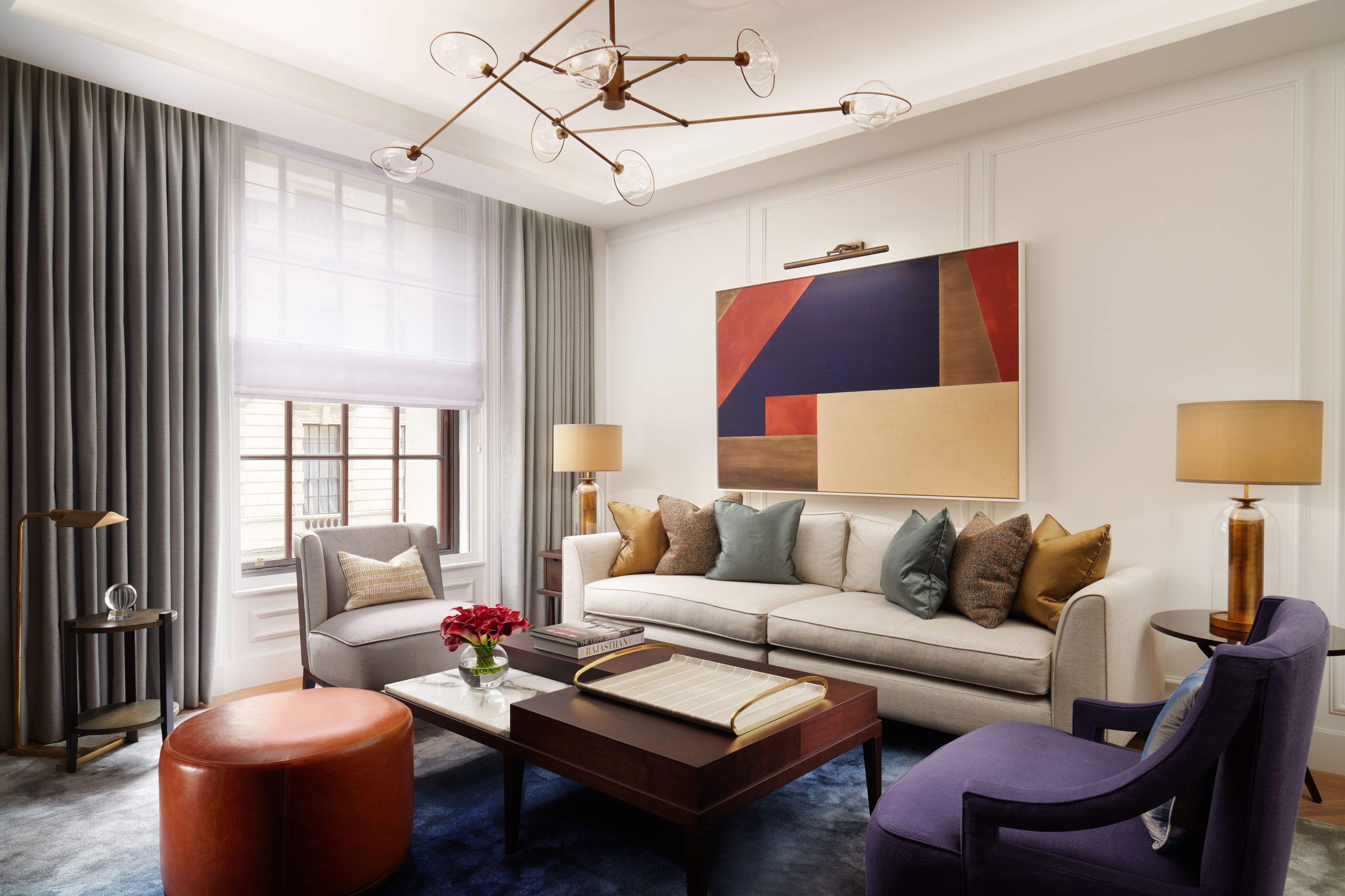A modern hotel room with a sofa, armchair, coffee table, and a large abstract painting on the wall.