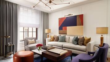 A modern hotel room with a sofa, armchair, coffee table, and a large abstract painting on the wall.