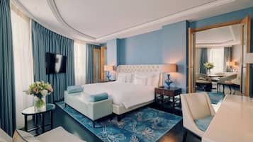 Una habitación de hotel moderna con una cama grande, una zona de estar con sofá y sillón, una mesa de comedor y un televisor.