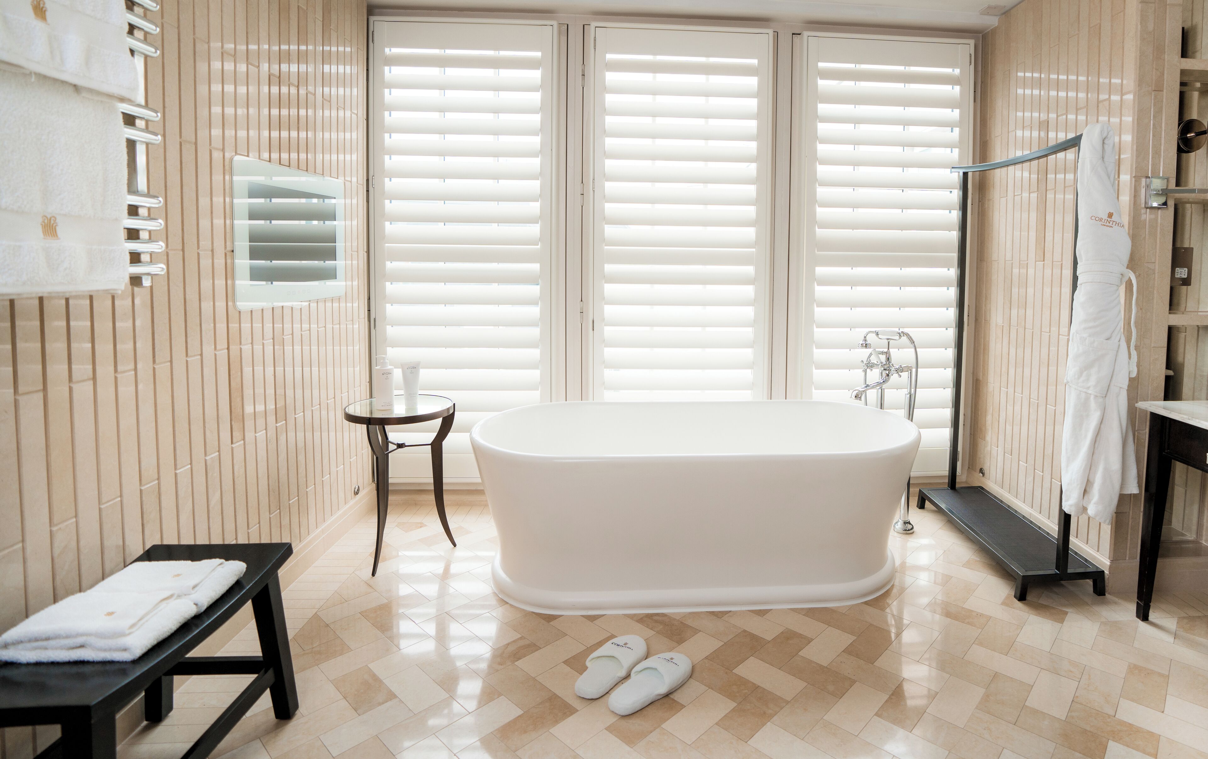 Une salle de bain moderne avec une baignoire sur pieds, une petite table ronde avec des articles de toilette et un banc.