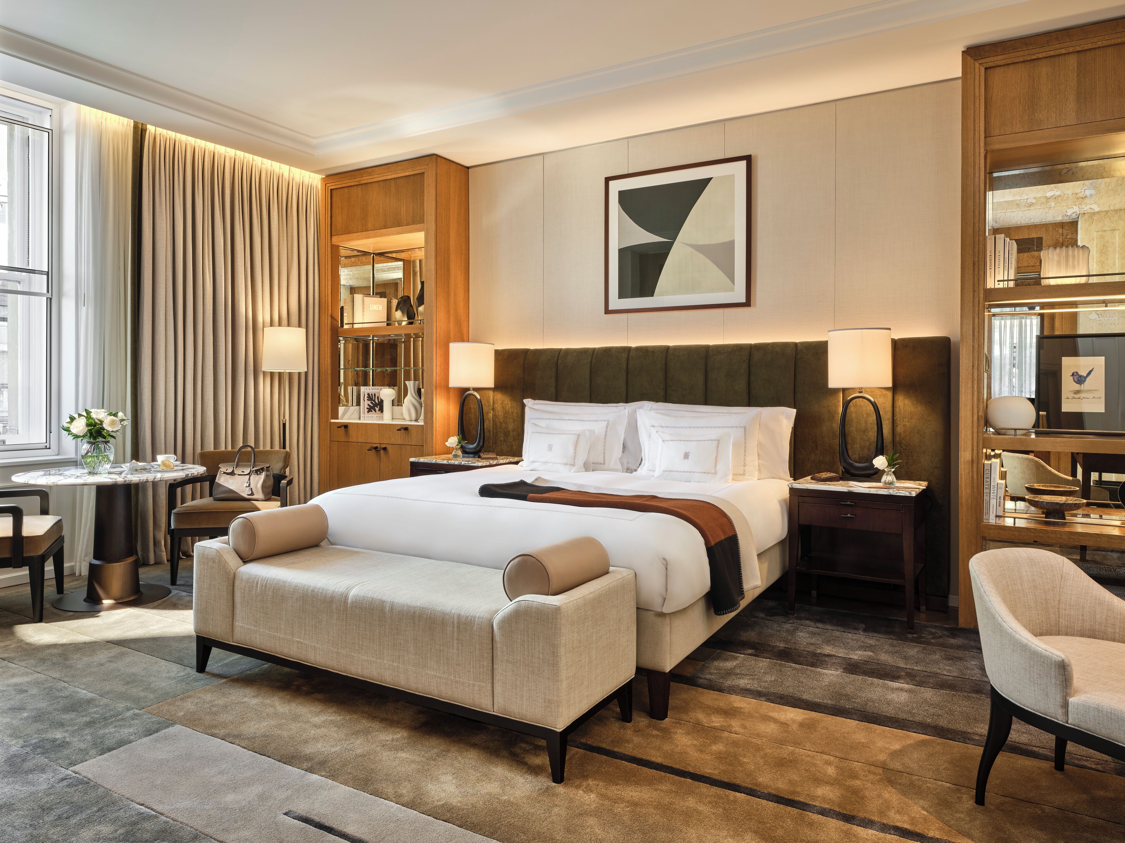 Habitación de hotel con una cama grande, una zona de estar con una silla y una mesa, un escritorio pequeño y una estantería.