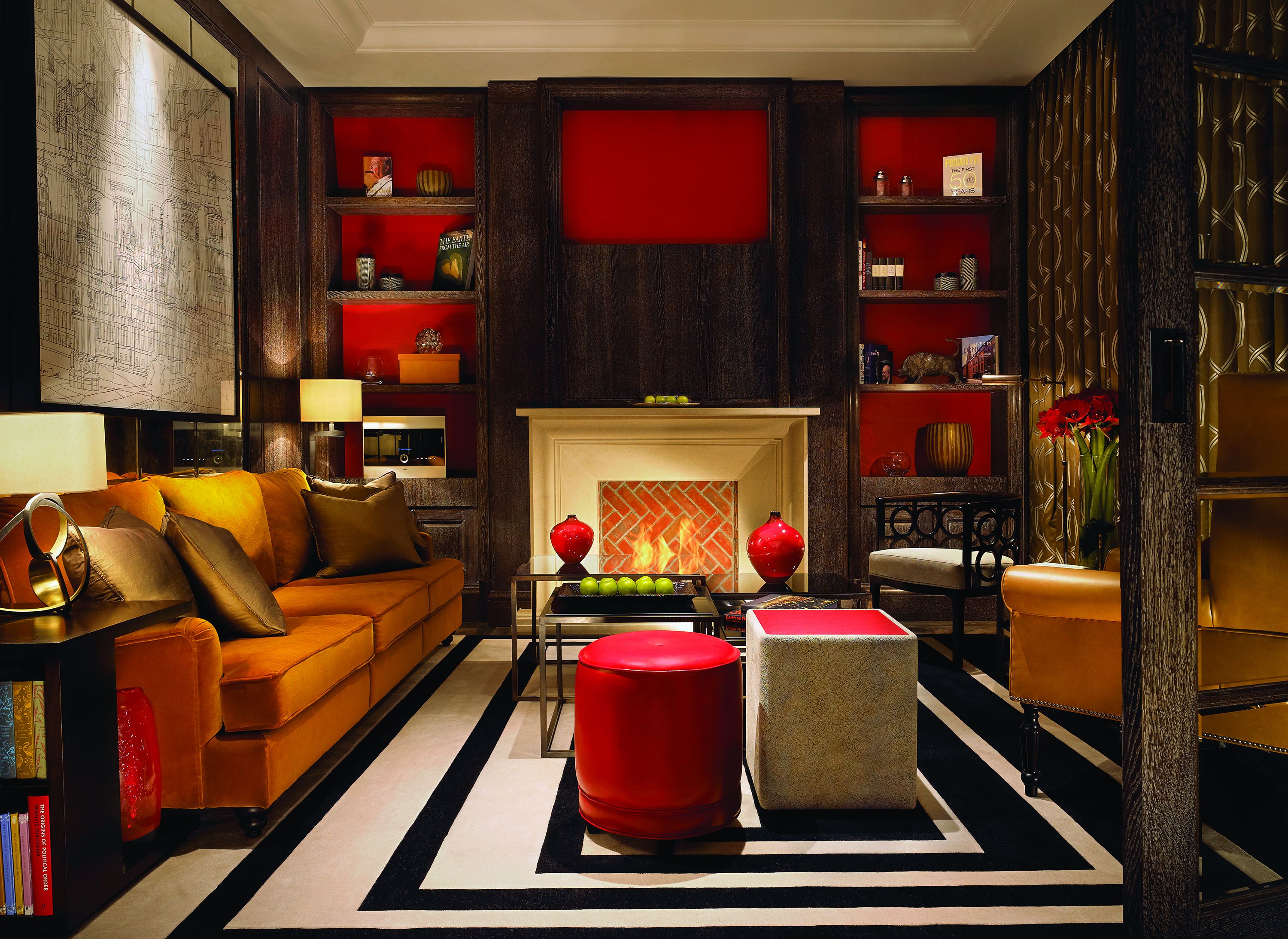 Un salon moderne avec une cheminée, un canapé, un pouf rouge et une bibliothèque.