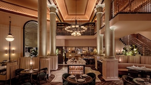 A spacious hotel lobby with a central dining area, multiple seating options, and a staircase leading to an upper level. - Corinthia London (London)