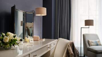 Een hotelkamer met een kaptafel, spiegel, lamp, stoel en raam met gordijnen.