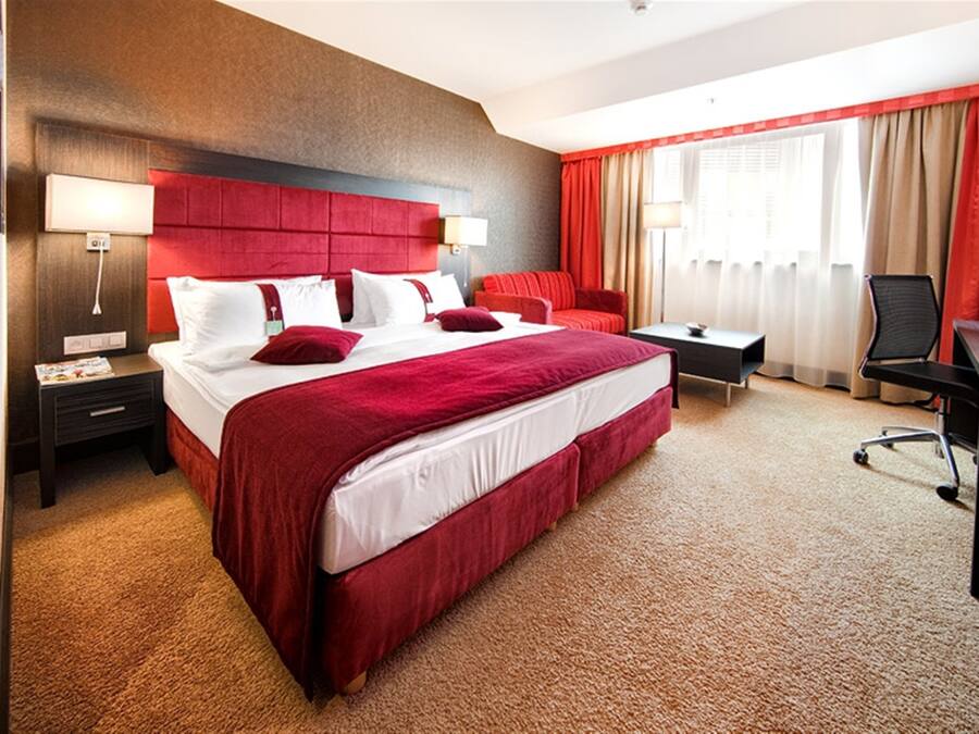 A hotel room with a large bed, a desk, a chair, a nightstand, and a lamp.