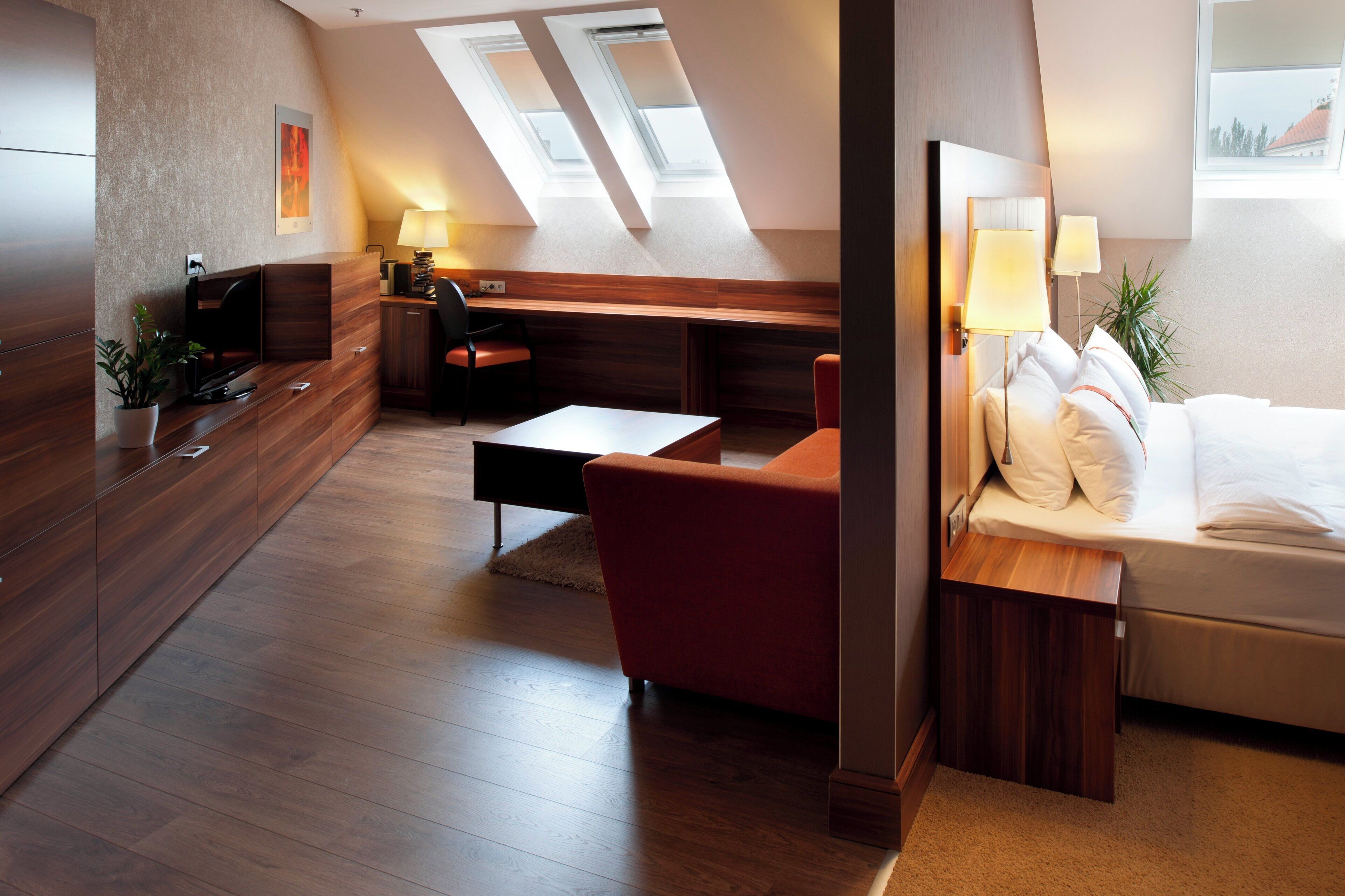A modern hotel room with a loft bed, a desk, a sofa, and a TV.
