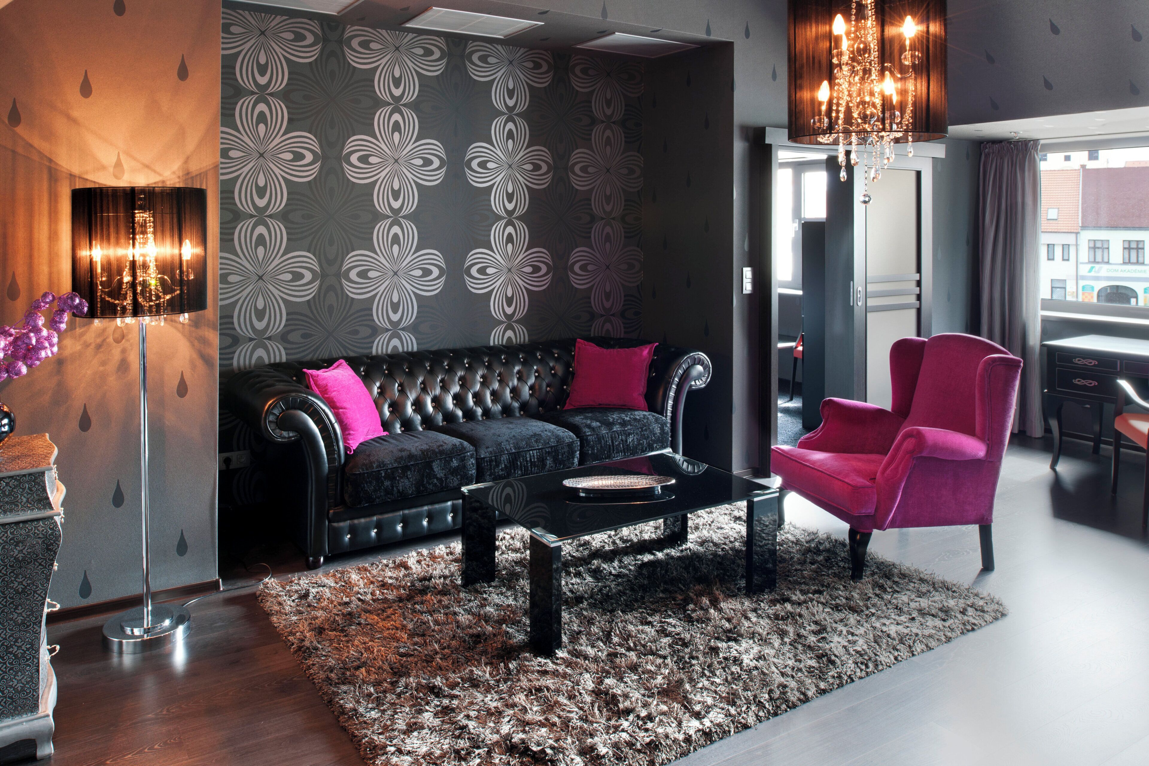 Una sala de estar moderna con un sofá capitonado, un sillón rojo, una mesa de centro de vidrio y una pared con diseño.