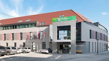 Un hotel Holiday Inn con diseño moderno, que cuenta con un techo rojo, ventanas amplias y un estacionamiento con varios autos.