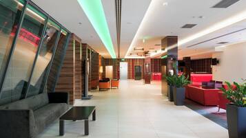 Un moderno vestíbulo de hotel con zona de estar, mostrador de recepción y una pantalla de televisión.