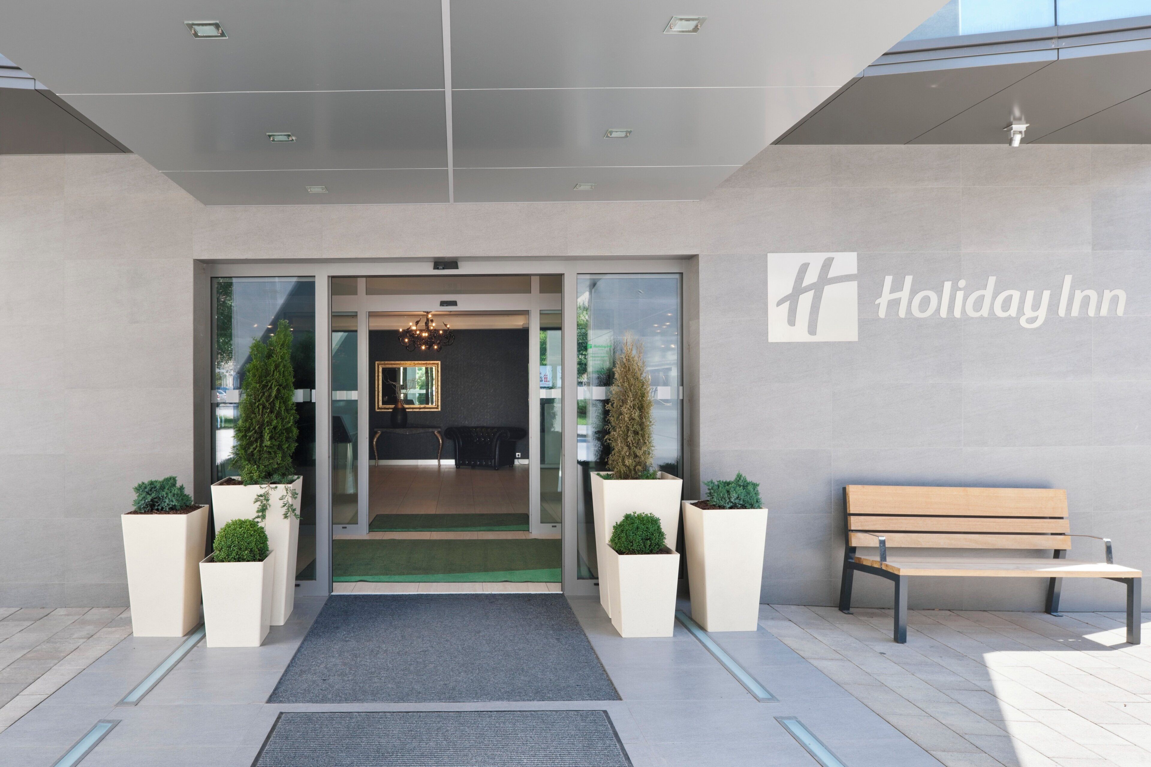 The entrance to a Holiday Inn with a bench and potted plants.