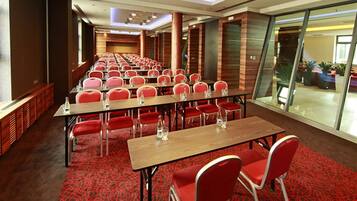 Un salón de conferencias con filas de mesas y sillas, una alfombra estampada y vistas a través de paredes de cristal.