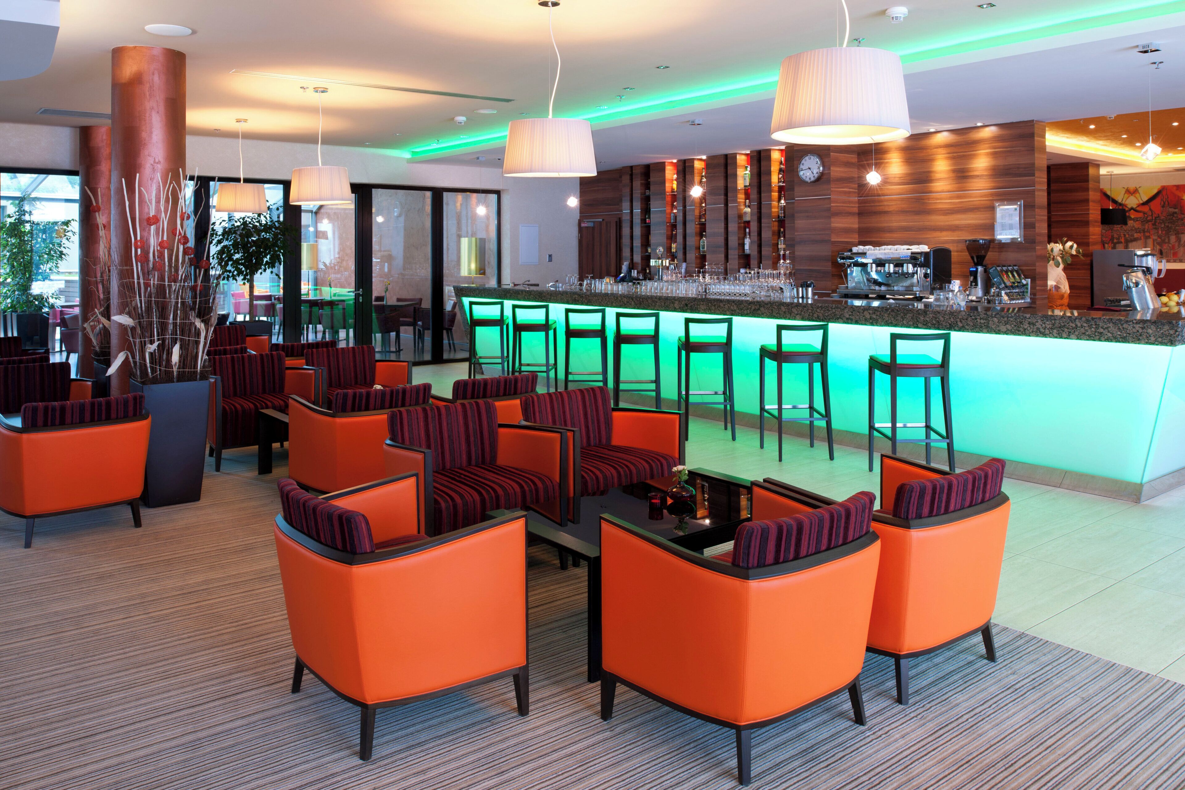 Un área de bar moderna con asientos naranjas, una barra y una máquina de café.