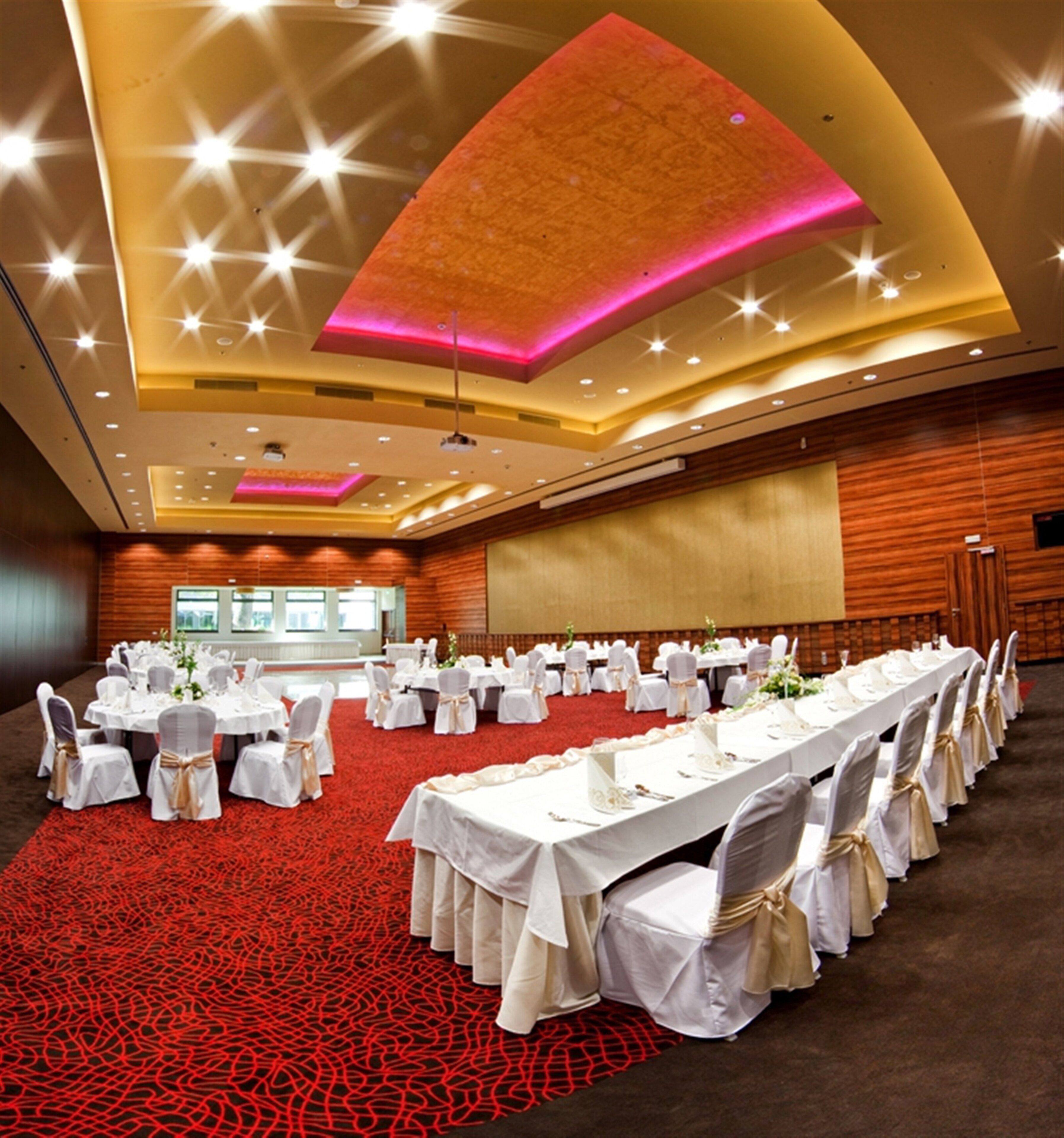 Un salón de conferencias con mesas redondas, manteles blancos y sillas con fundas blancas.