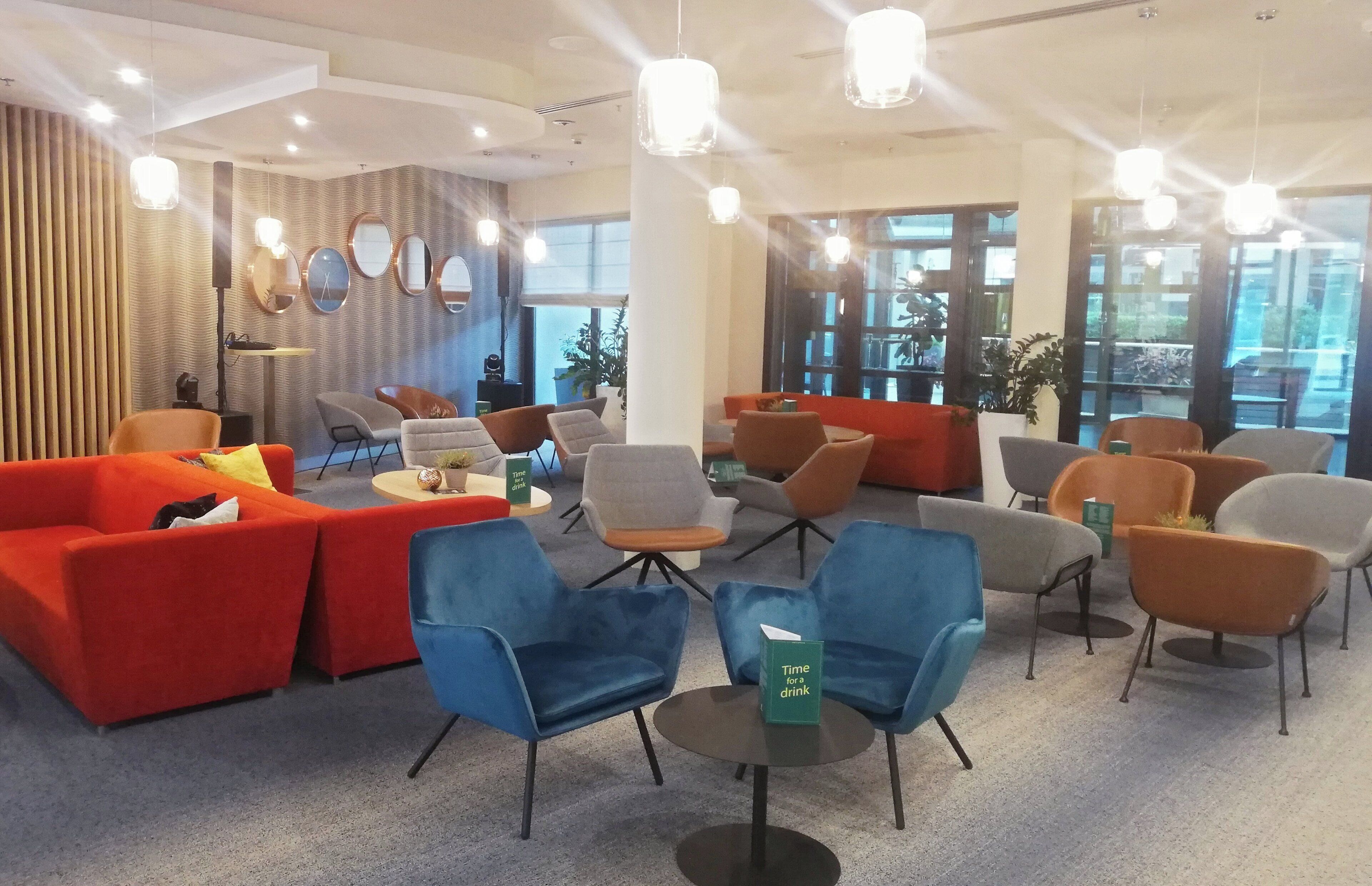 A modern lounge area with sofas, chairs, and a coffee table, featuring a large window and ceiling lights.