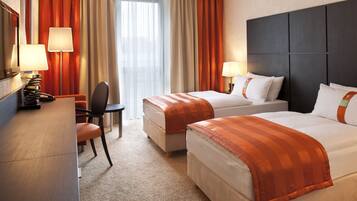 A hotel room with two beds, a desk, a chair, and a desk lamp.