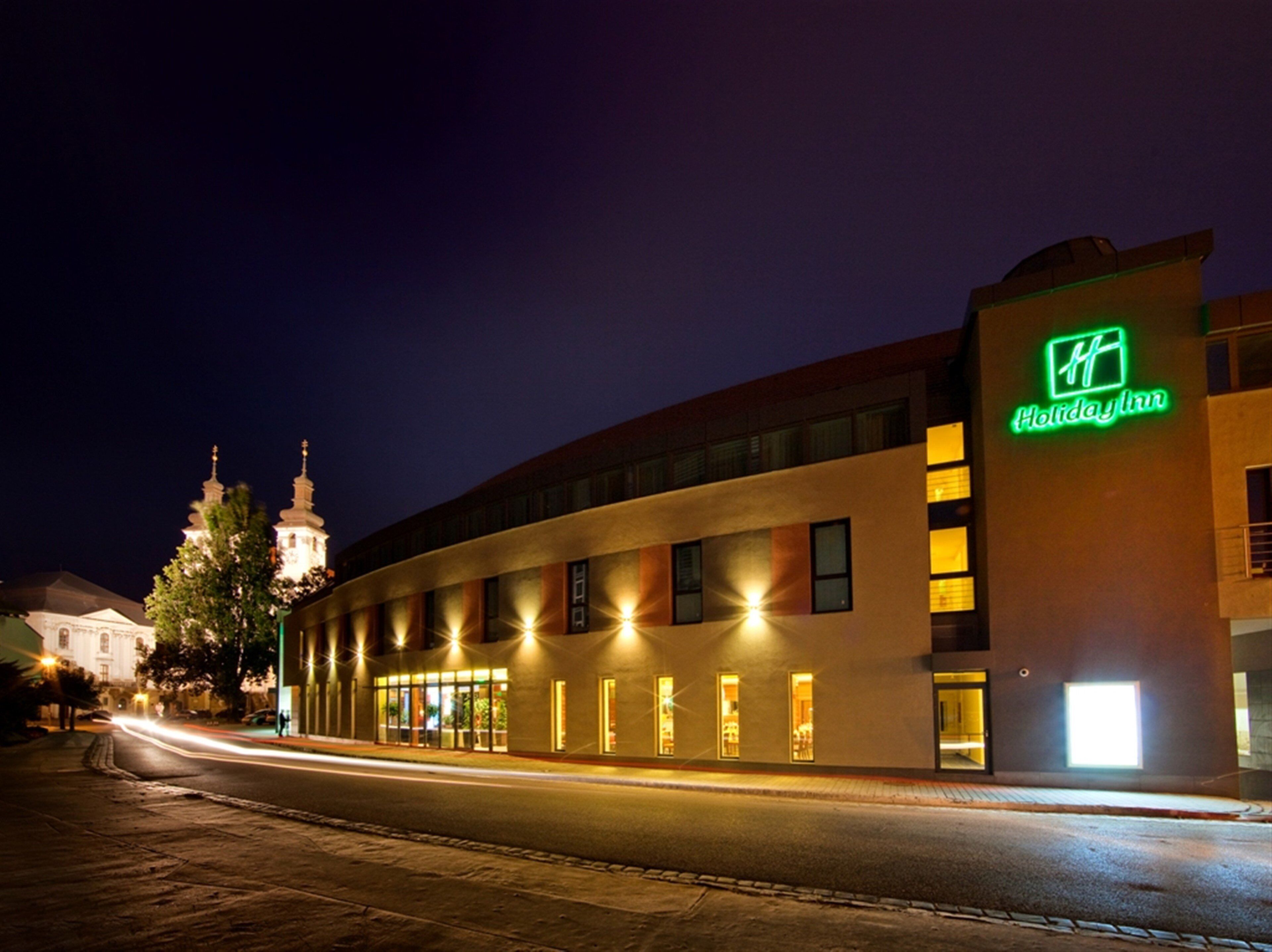 A Holiday Inn hotel with a modern design, featuring a prominent neon sign, a curved facade, and a well-lit entrance.