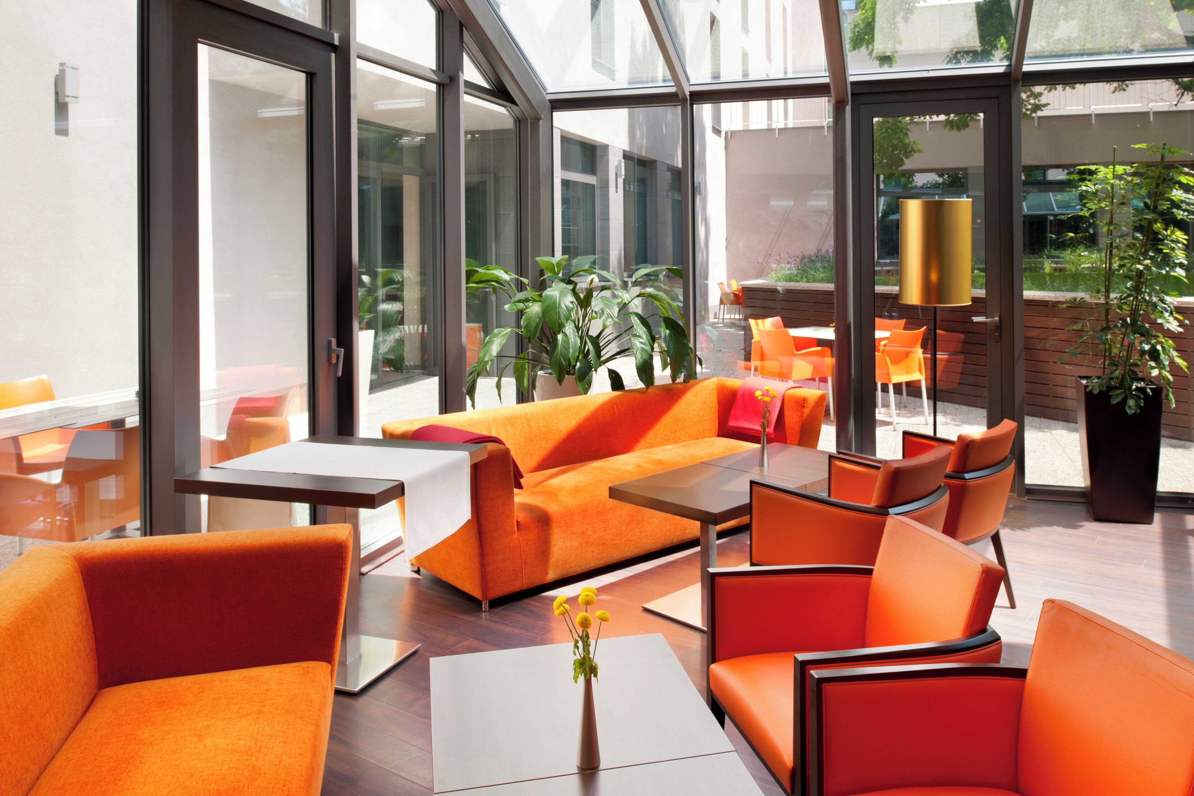 A modern indoor seating area with orange furniture, large windows, and indoor plants.