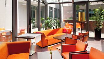 Un área de estar interior moderna con muebles anaranjados, ventanas amplias y plantas de interior.