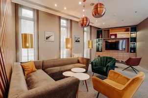 Una sala de estar moderna con un sofá marrón, dos mesas redondas blancas y sillas de colores.