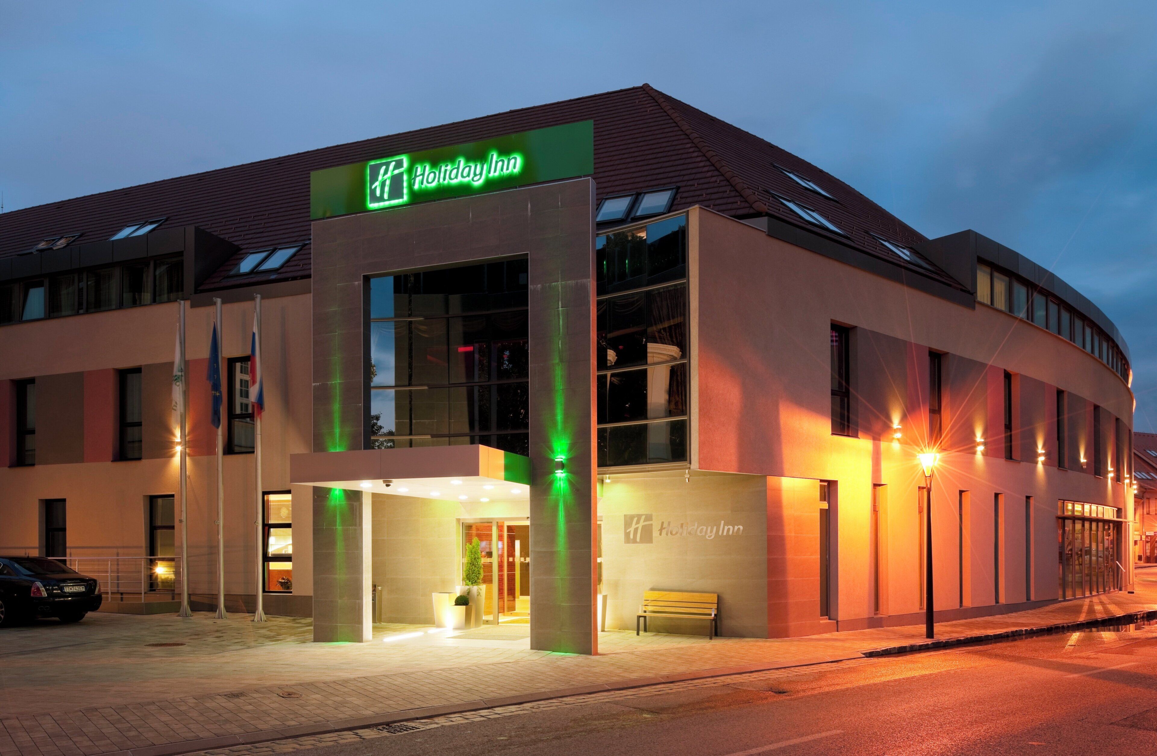 Un hôtel Holiday Inn au design moderne, caractérisé par une enseigne verte bien visible, de grandes fenêtres et une entrée bien éclairée.