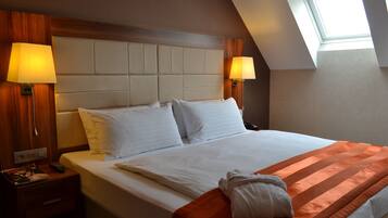Camera d'albergo con un letto grande, due lampade ai comodini, una testiera in legno e un lucernario.