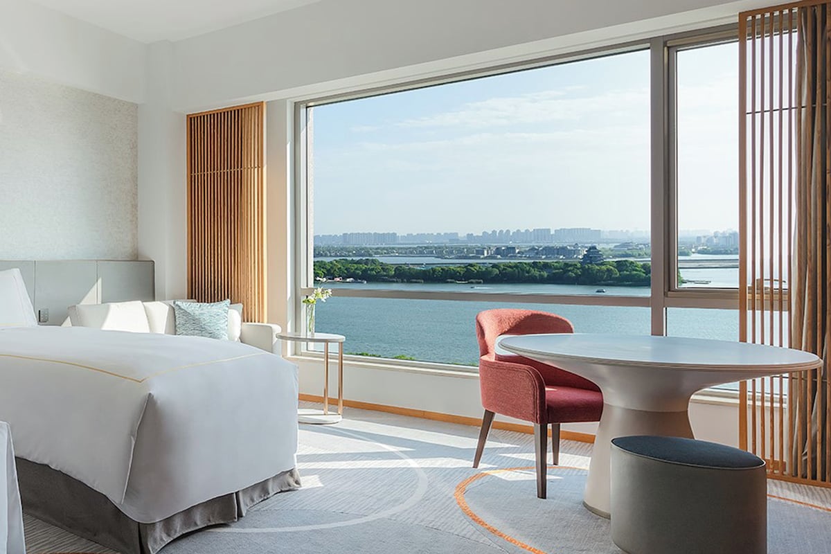 A hotel room with a bed, a table, a chair, and a view of a river.