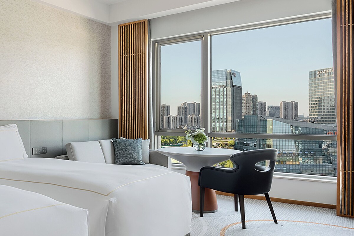 Habitación de hotel con una cama grande, un escritorio y vistas a la ciudad.