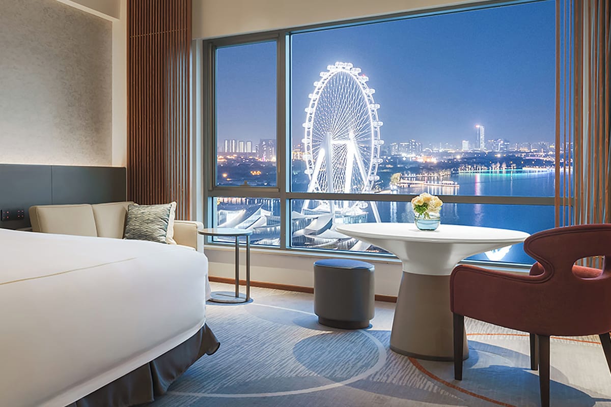 A hotel room with a large bed, a seating area, and a view of a Ferris wheel.