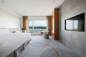 A modern hotel room with a large bed, a desk, a chair, and a TV mounted on the wall.