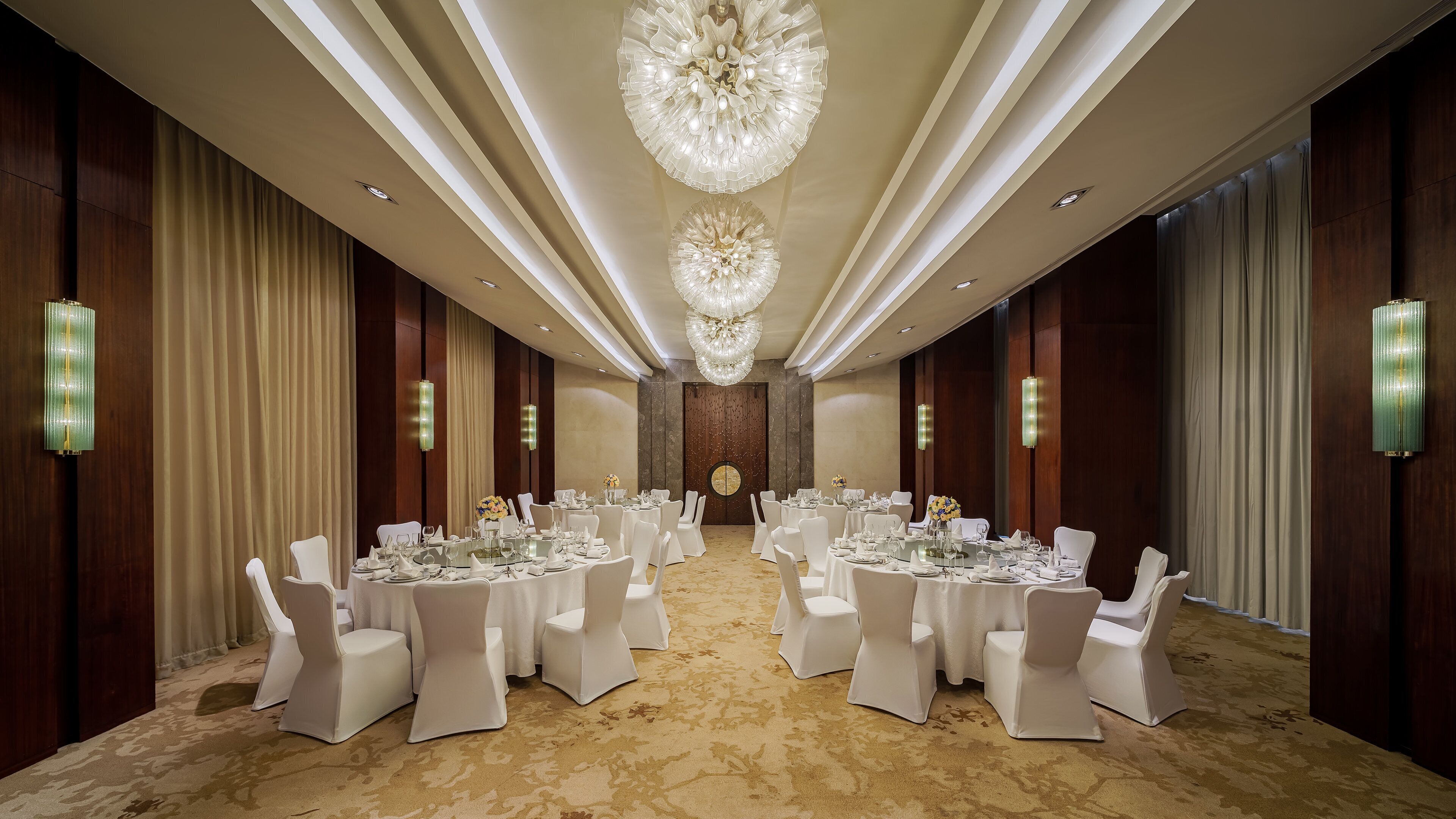 Een feestzaal met ronde tafels, witte stoelen en een grote kroonluchter.