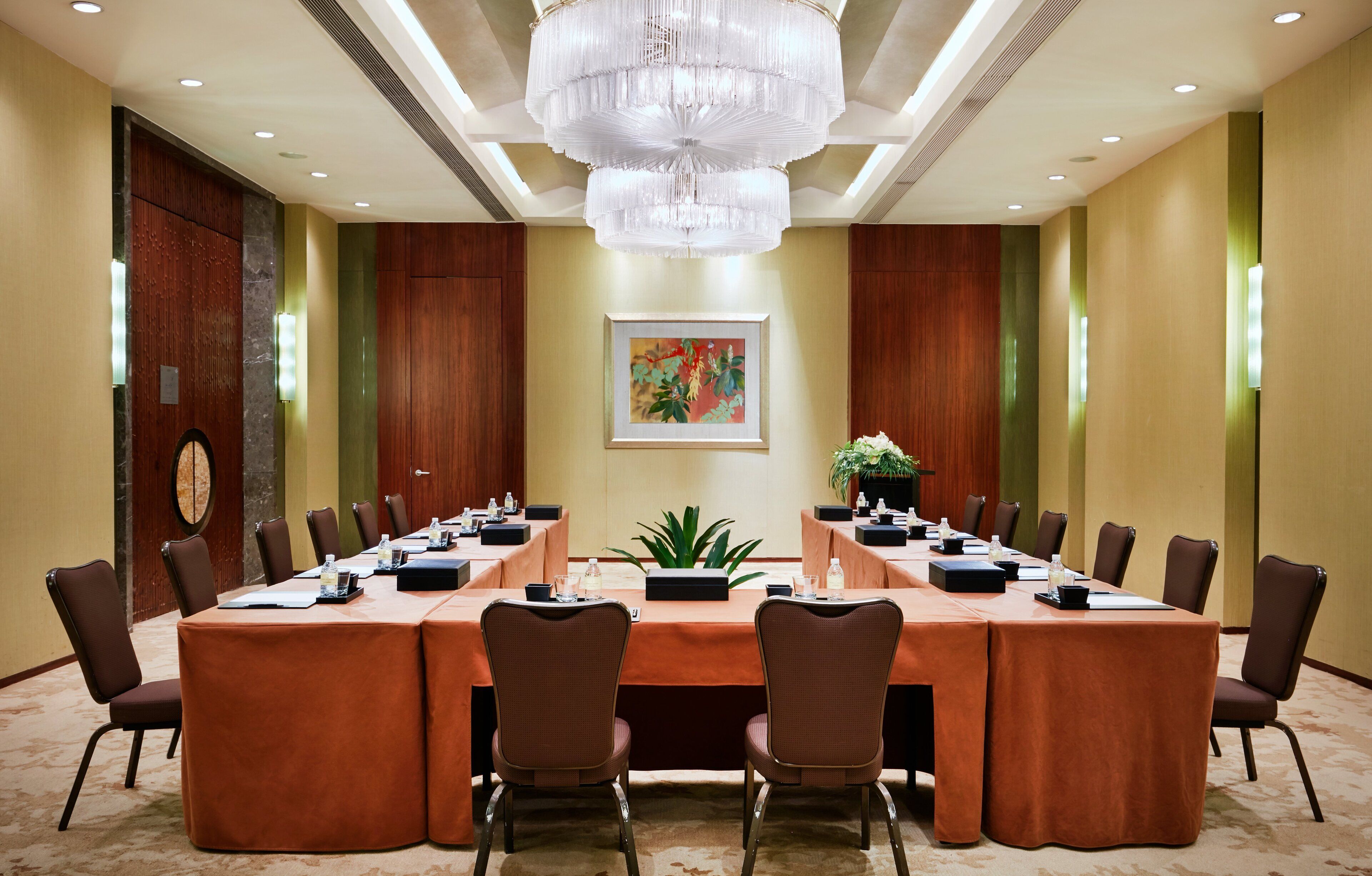 A conference room with a long table, chairs, a chandelier, and a framed picture on the wall.