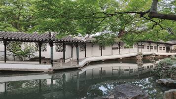 A traditional Chinese garden with a stone bridge over a pond, surrounded by lush greenery and classical architecture.