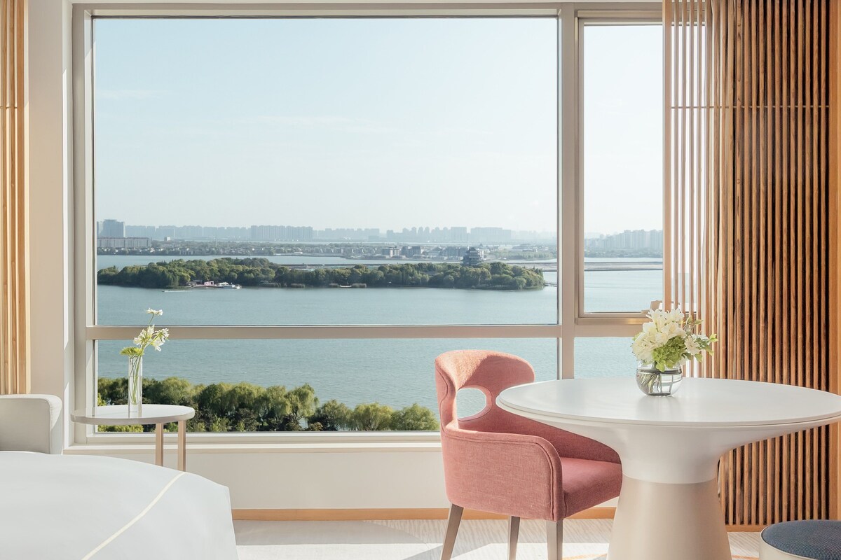 Habitación de hotel con un ventanal grande que ofrece vistas a un río y al paisaje urbano.