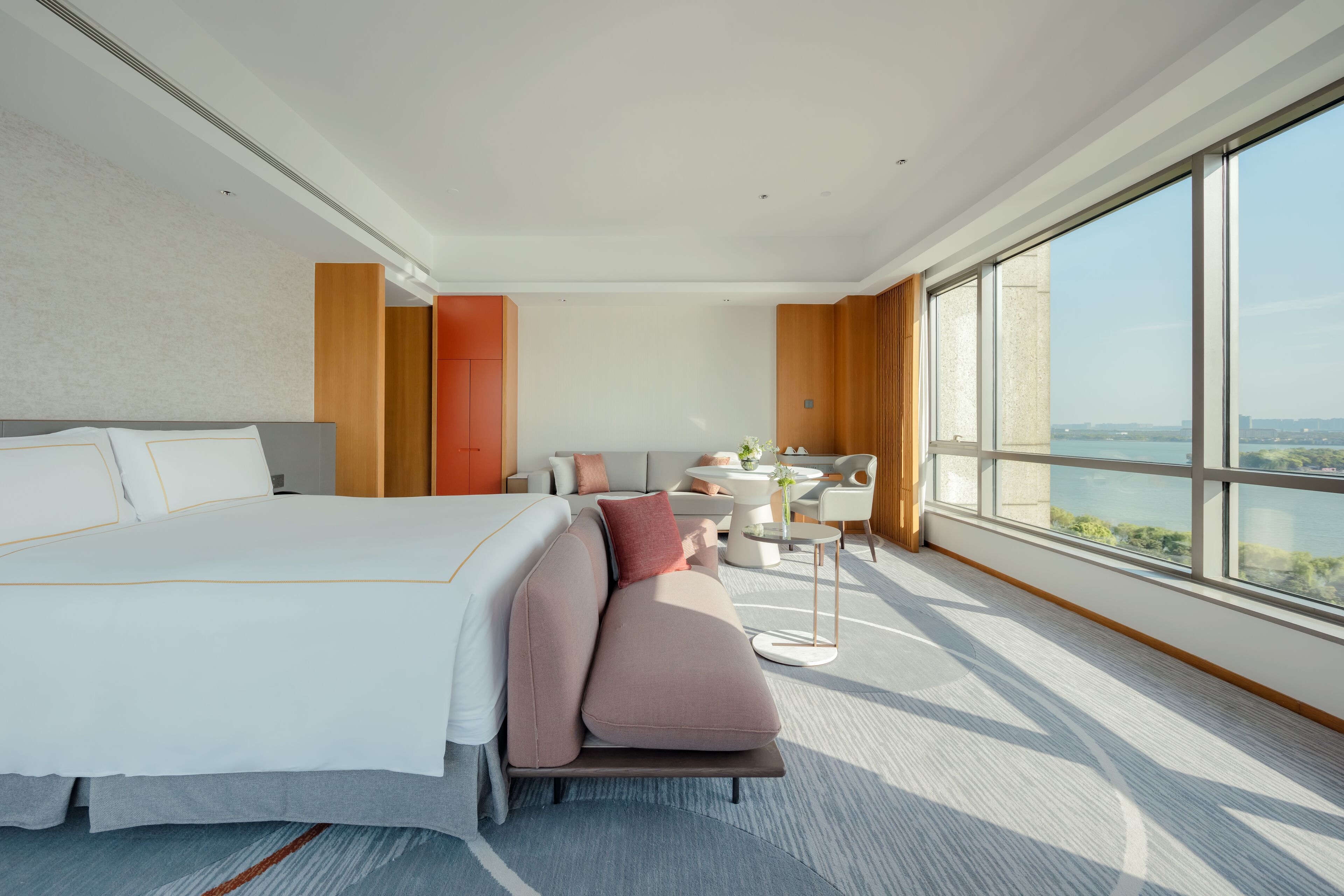A modern hotel room with a large bed, a sofa, a desk, and a view of the city.