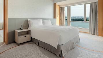 A hotel room with a large bed, a nightstand, a view of a body of water, and a cityscape.